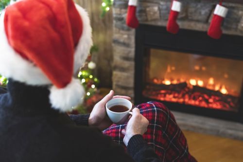 A man wearing a santa hat sits alone at a fireplace thinking about his holidays after divorce
