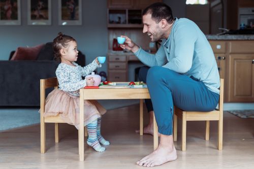 Profile view of a dad and his toddler daughter sitting at a child size table and having a tea party. Visual concept for legal advice blog discussing tips for helping younger children cope with separation and divorce.