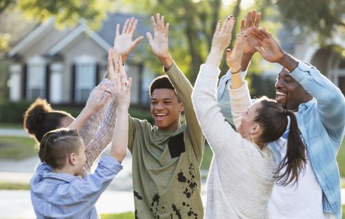 A multi-ethnic blended family of five, with three children, dancing together in their front yard. Visual concept for a blog discussing tips for a happy blended family.