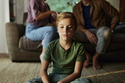 Sad little boy sitting in front of his parents who are arguing at home. Visual concept for blog discussing divorce with kids.