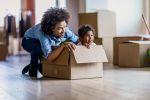 Happy single mother and her small daughter in cardboard box at their new home.