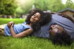 African-American son and father rests on grass enjoying time together.