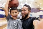Father laughs and takes a selfie while his son holds a basketball on his head. Concept for Choosing a Guardian for Your Children.