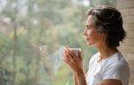 Sad Latin American woman drinking a cup of coffee while looking out the window. Visual concept for legal blog discussing how to divorce a missing spouse legally.